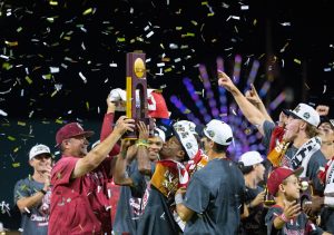 Oklahoma head coach Skip Johnson, front left, hands the championship trophy to Jason Walk, center, as they celebrate after their victory over North Carolina in Game 3 of the NCAA College World Series baseball finals in Omaha, Neb., Monday, June 22, 2026. (AP Photo/Rebecca S. Gratz)